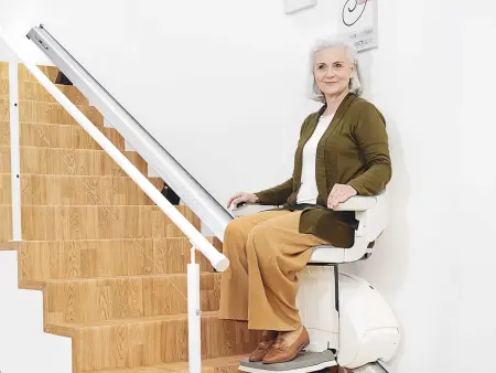 A woman sits on a white stair lift halfway up a staircase in a bright, modern home. 